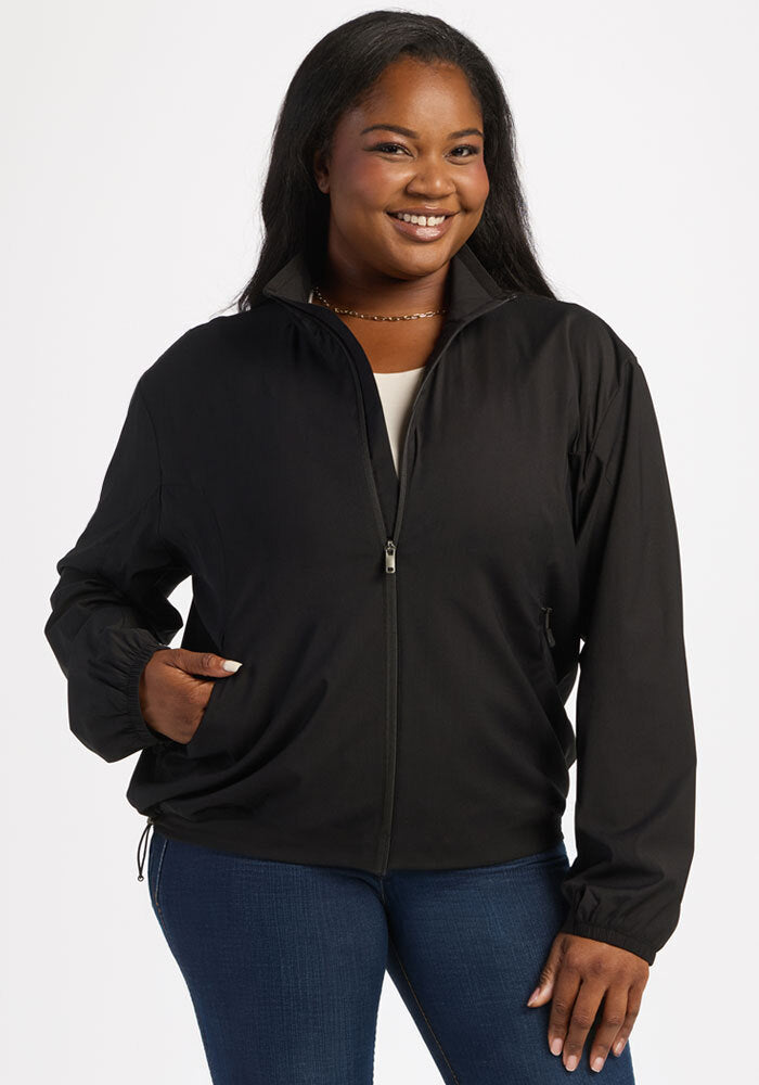 Woman in Woolx Cooper Windbreaker - Black and blue jeans, smiling with a hand in her pocket against a white background.