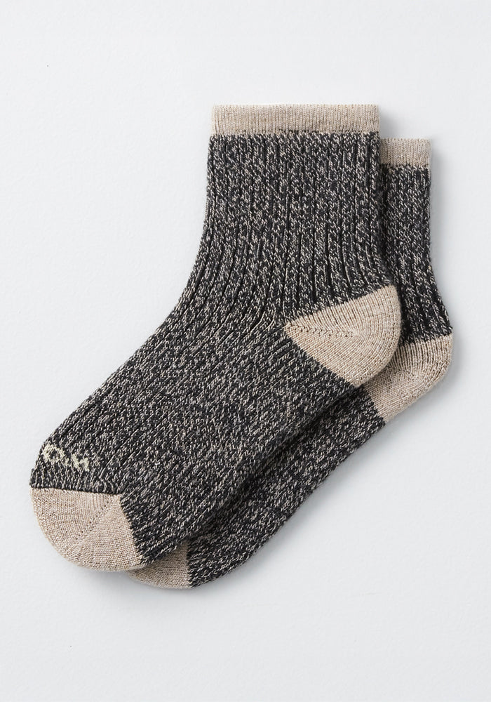 The Womens Cozy Mini Crew Sock by Woolx features a black and white marled ribbed design with beige toes, heels, and cuffs. Shown ankle-length and laid flat against a light background.
