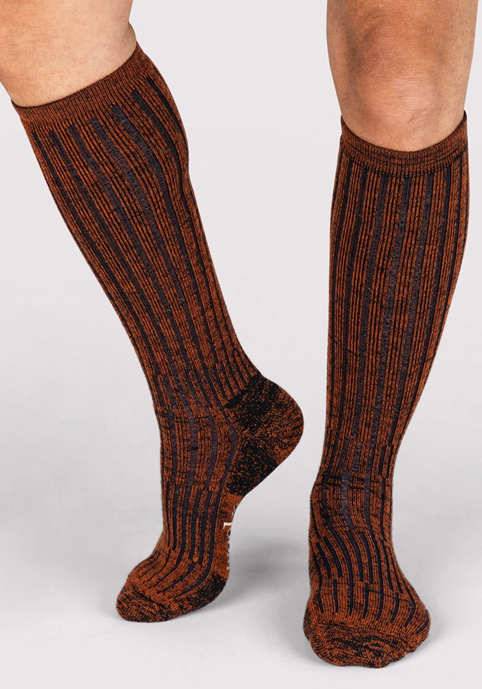 A person wearing Woolx Mens Joey Mid Calf Socks in Cinnamon Spice stands on a light gray surface.