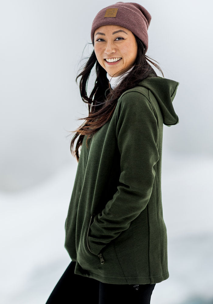 Woman in Woolx Cubby Hooded Sweatshirt - Duffel Bag smiles outdoors, snowy backdrop softly blurred behind her.