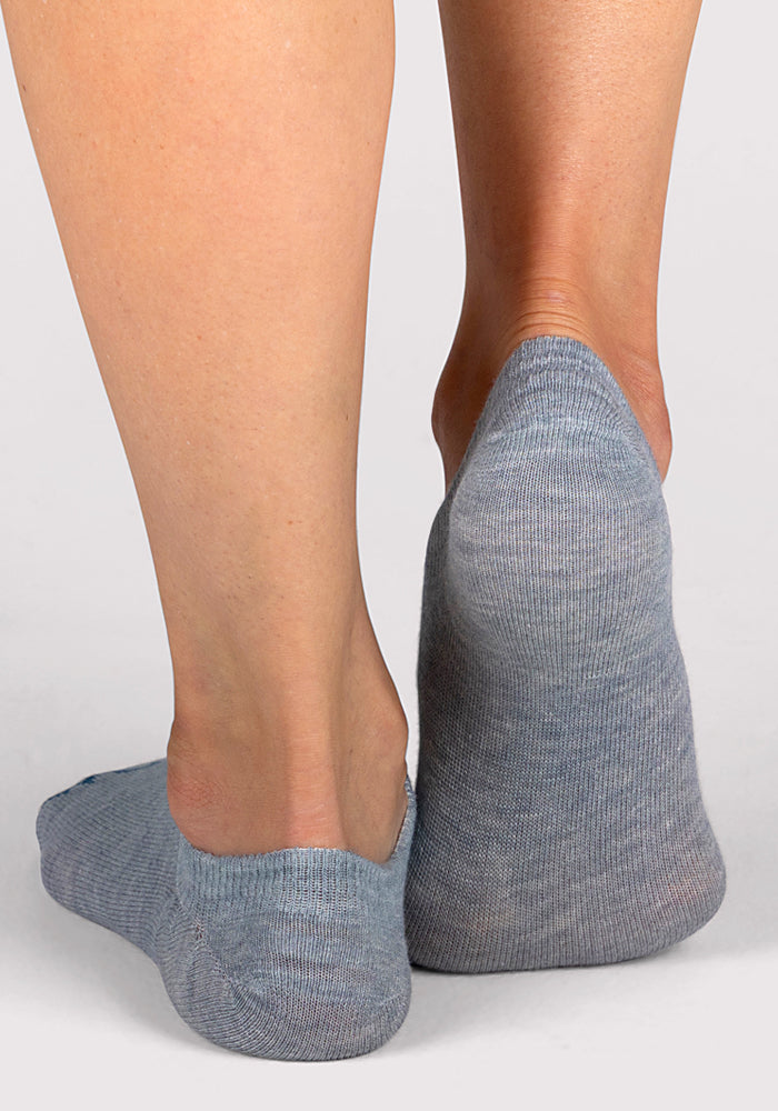 A pair of feet wearing Woolx Womens Daisy Ped Socks in Calm Waters, one heel lifted and the other foot flat against a plain light background. Perfect for everyday comfort.