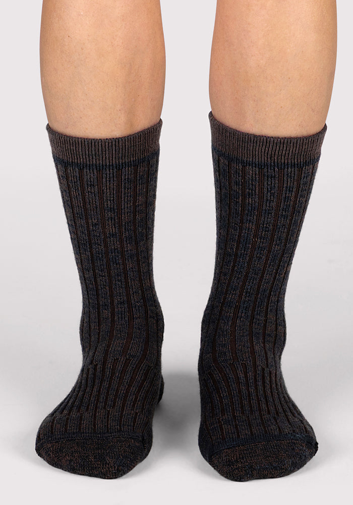 A close-up of a person’s lower legs wearing Woolx Womens Joey Crew Socks in Dark Espresso, featuring a subtle striped pattern and standing on a light gray surface.