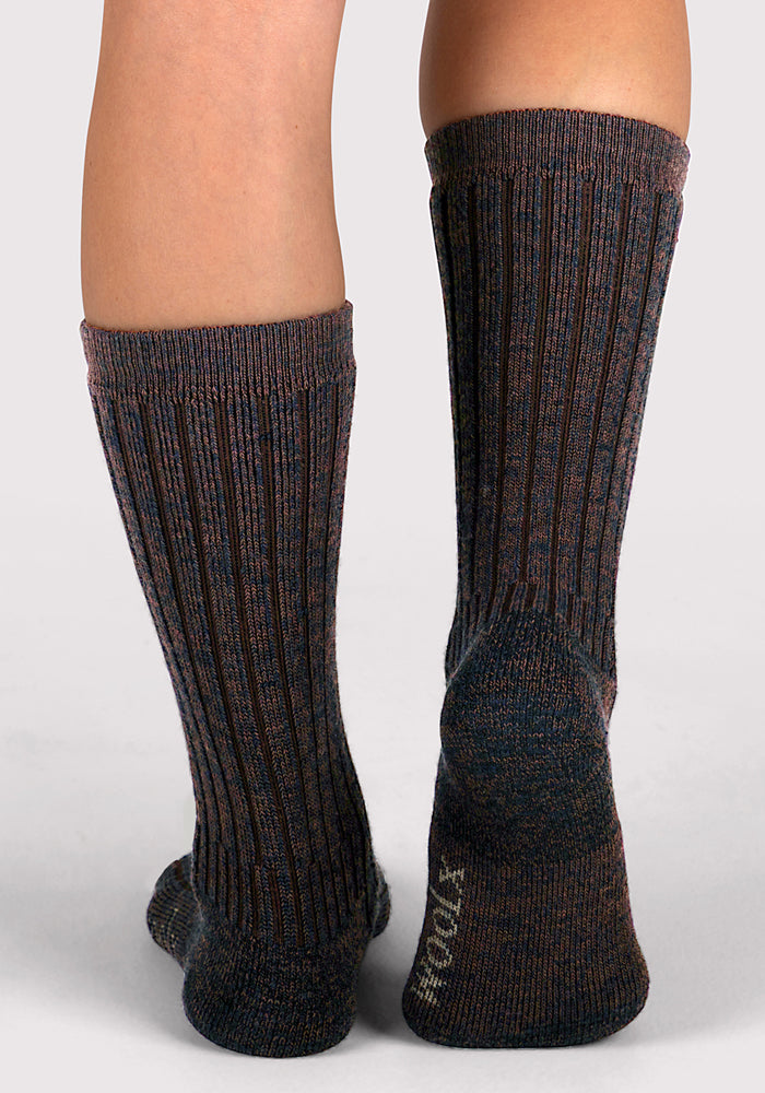 A close-up of a person wearing Woolx Womens Joey Mid Calf Socks in Dark Espresso, featuring ribbed, multi-colored fabric and "SOCKS" printed on the sole, standing against a neutral background.