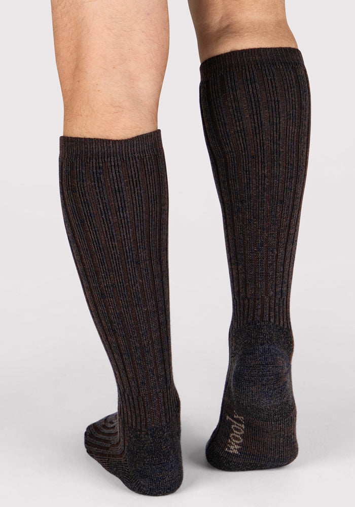 A person wears Woolx Mens Joey Mid Calf Socks in Dark Espresso, standing on a light background with the back and side of their lower legs and feet visible.