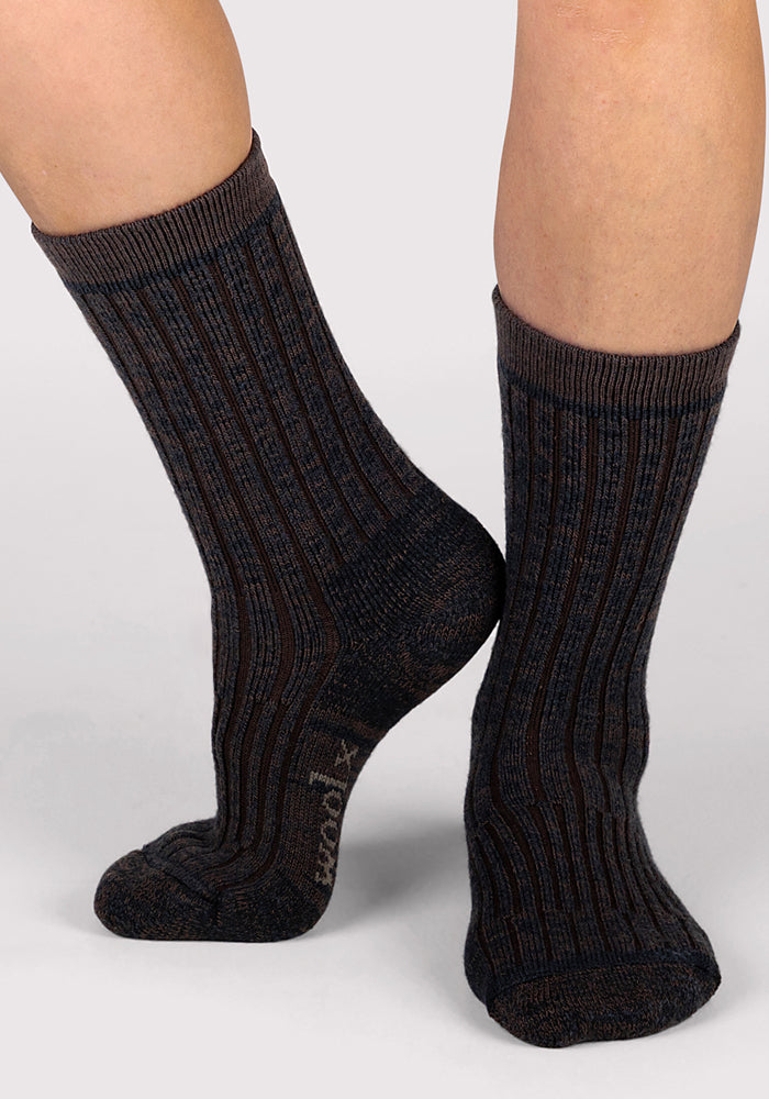 A person wearing Woolx Womens Joey Crew Socks in Dark Espresso stands on a light background, one foot flat and the other slightly raised.