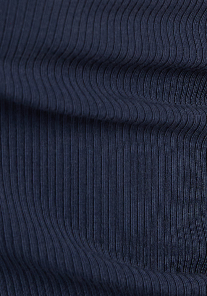 Close-up of the Woolx Iris Ribbed Dress in Deep Navy, highlighting its ribbed knit fabric with vertical textured lines that create a wavy pattern across the surface.