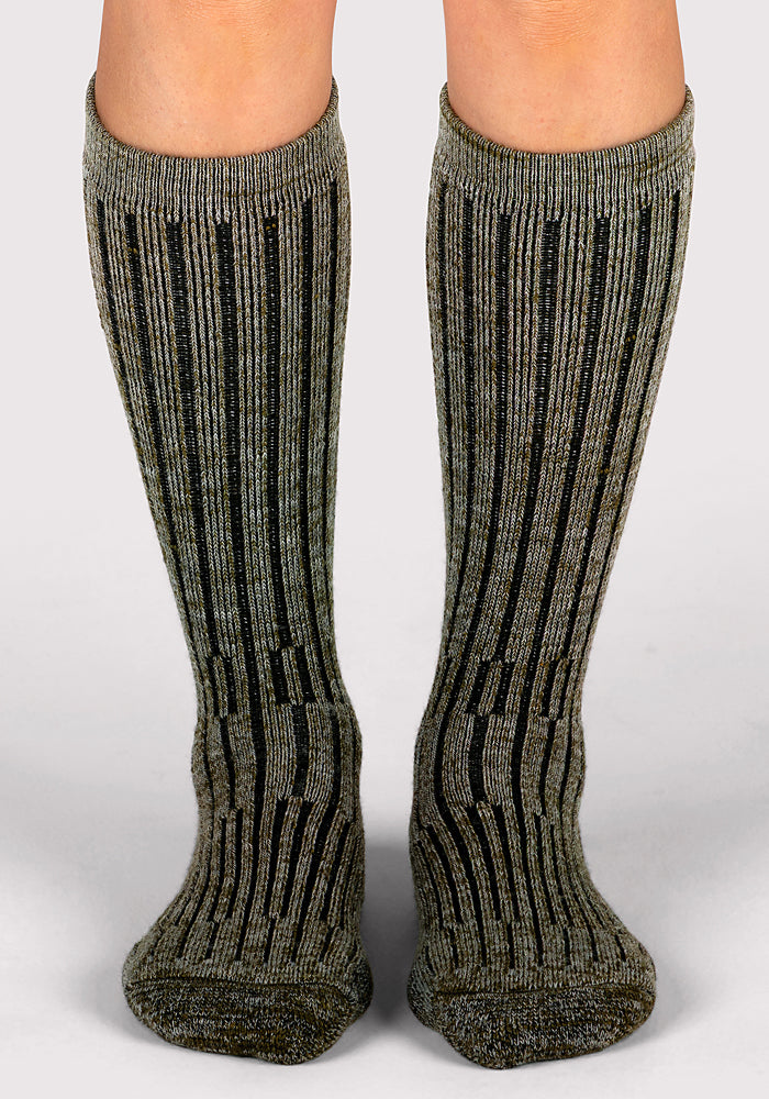 A close-up of two legs wearing Woolx Womens Joey Mid Calf Socks in Dark Forest Marled, standing on a light gray surface.