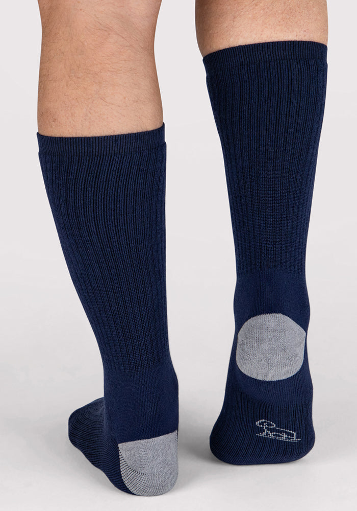 A pair of legs wearing Woolx Mens Core Crew Socks in Deep Navy with gray heels and toes, shown from the back. These moisture-wicking socks have a small white embroidered logo near the heel for added style and comfort.