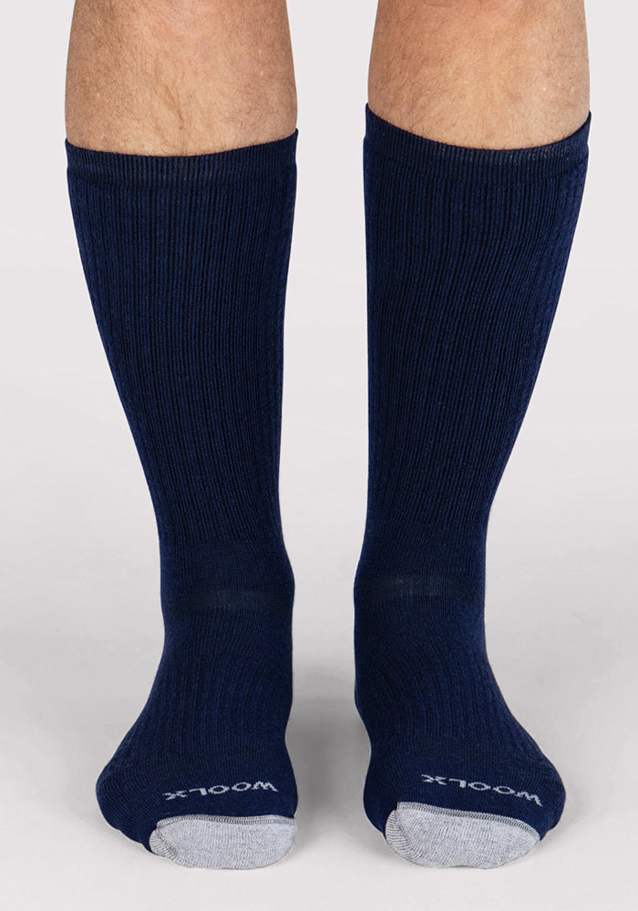 A person wearing Woolx Mens Core Crew Socks in Deep Navy with ribbed merino wool, light gray toes, and "Woolx" on the toe stands on a light background. These moisture-wicking socks provide all-day comfort and performance fit.