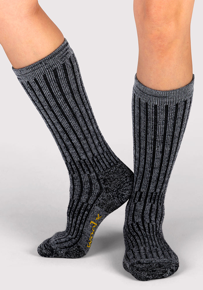 A person wearing Woolx Womens Joey Mid Calf Socks in Dark Navy Marled stands on a light gray background.