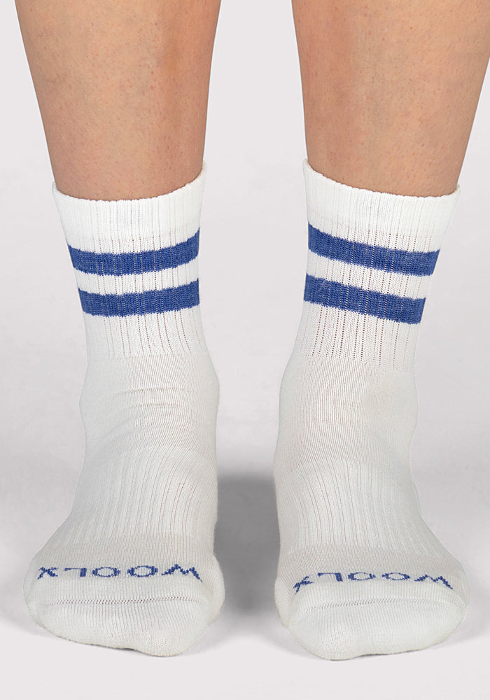 A pair of feet wear Woolx Womens Varsity Mini Crew Socks in Electric Blue, featuring two blue stripes near the top and blue "WOOLX" text on the toes, photographed against a plain background. Stylish merino wool crew socks with breathable comfort.