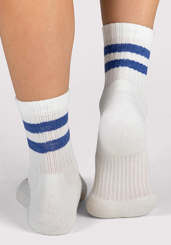A close-up of two feet standing on a light surface, wearing Woolx Womens Varsity Mini Crew Socks in Electric Blue with two horizontal blue stripes near the top.