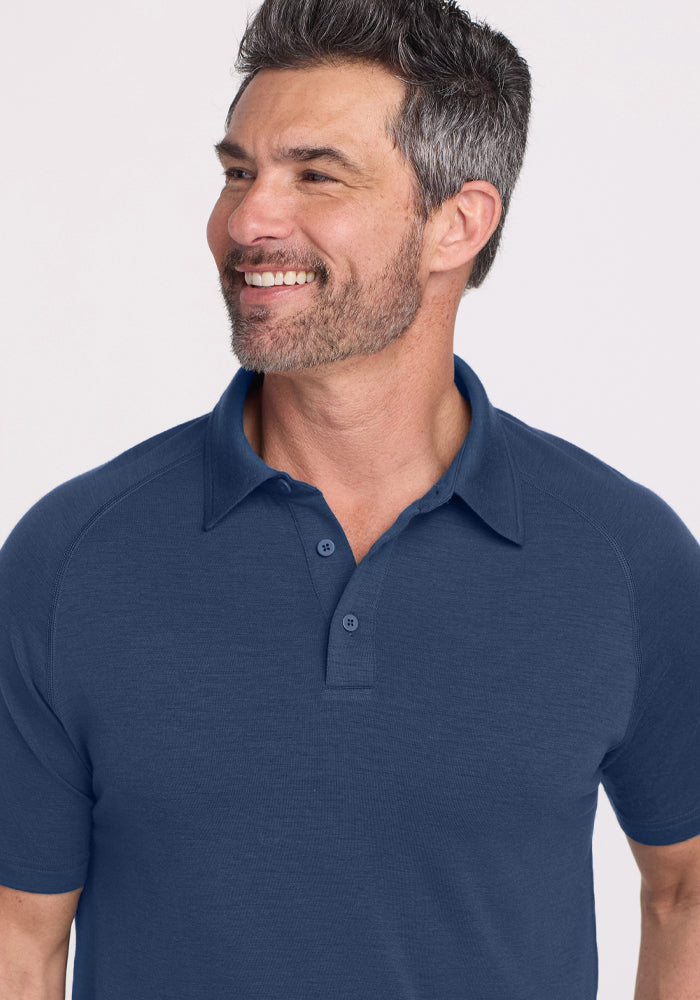 A smiling man with short salt-and-pepper hair and a trimmed beard wears the Woolx Summit Polo in Starry Night, looking off to the side against a light background.