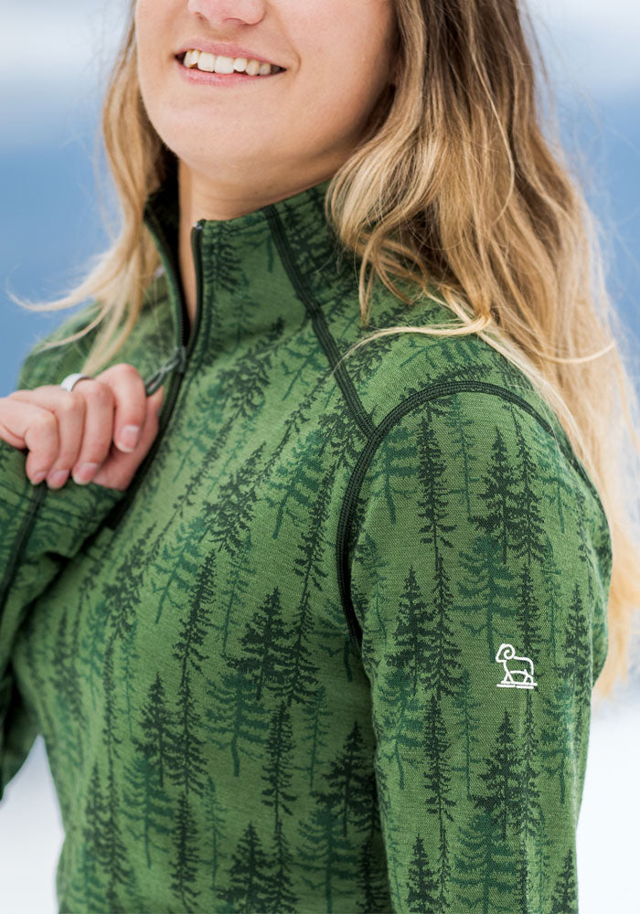 Smiling woman in Woolx Emi 1/4 Zip - Forest Friends jacket, featuring a black tree pattern and logo on the sleeve.