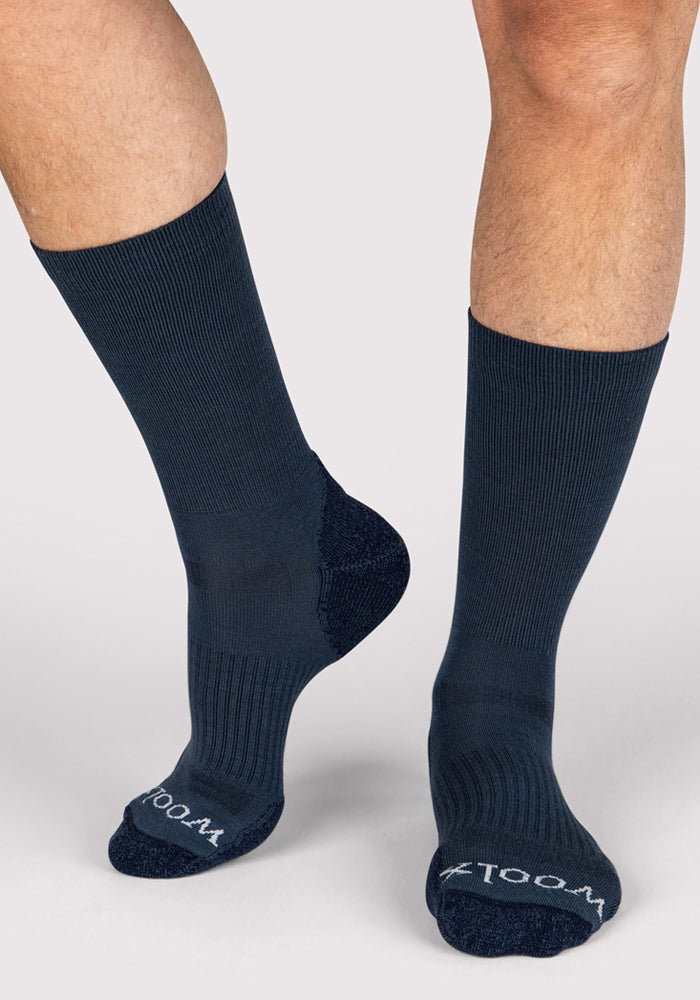 A person models Woolx Mens Harbor Crew Sock in Evening Tide, featuring a ribbed texture and "WOOL" visible on the toes. The moisture-wicking, calf-length Merino wool socks are shown against a light gray background.