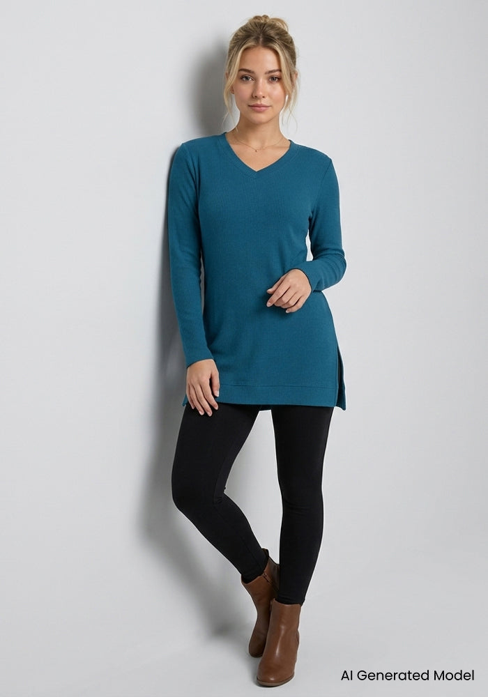 Woman in a Woolx Evie Petite Tunic - Blue Pine, black leggings, and brown boots stands by a light gray wall.