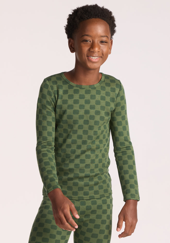 A smiling child wearing the Woolx Kids Explorer Base Layer Top in Frog Hop stands against a plain light background. 