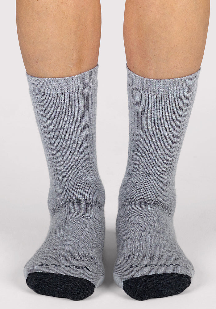 A pair of feet in Woolx Womens Core Crew Socks - Grey, featuring black toes, stand on a light surface. The socks look thick, comfortable, and perfect for long hikes.