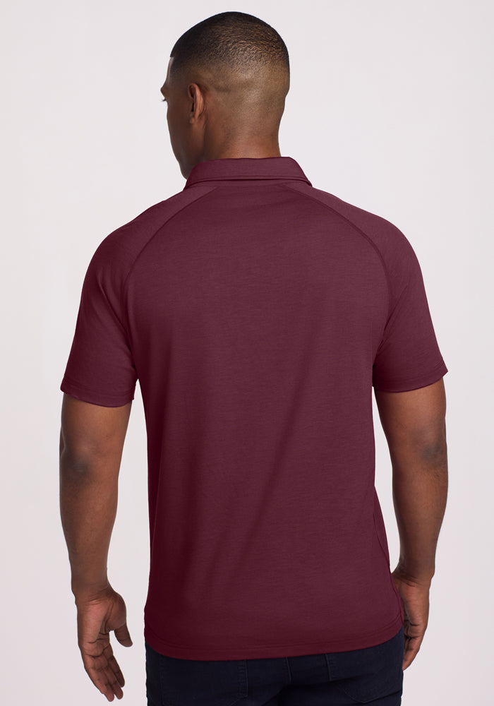 A man stands with his back to the camera, wearing the Woolx Summit Polo in Grape Harvest with dark pants against a light background.