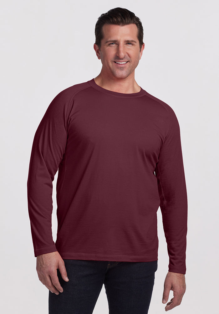 A man with short brown hair stands smiling in a Woolx Essential Tee - Grape Harvest and dark jeans against a plain light background. 