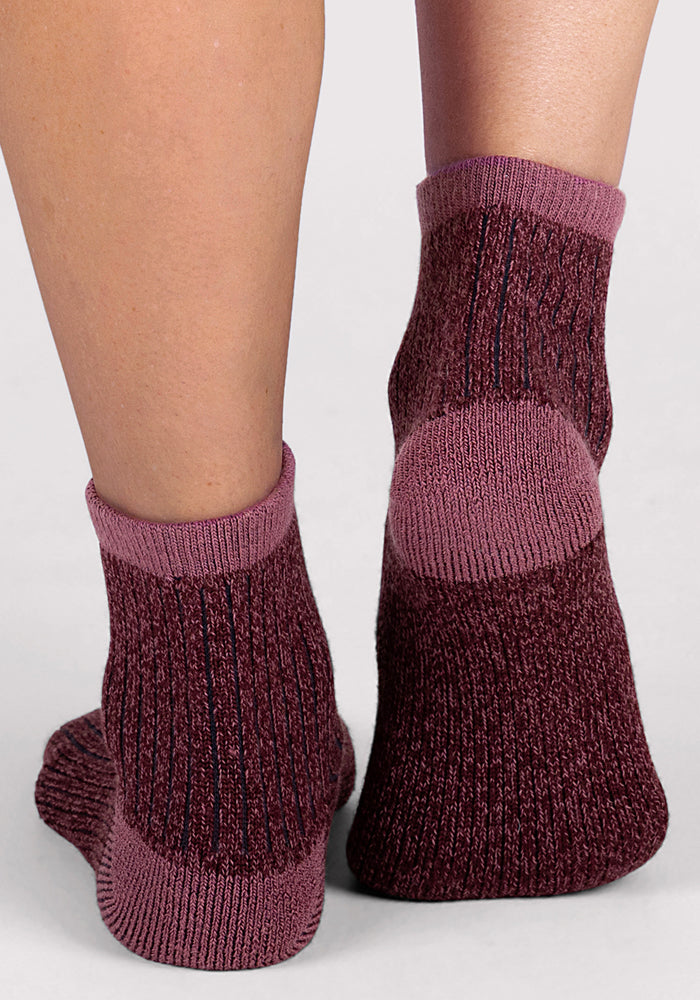 A close-up of two feet in Woolx Womens Cozy Mini Crew Sock - Grape Harvest, featuring thick burgundy and purple Merino wool, shown from behind on a light gray background.