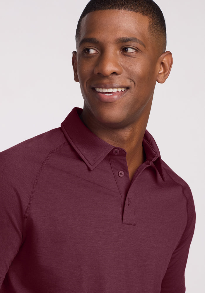 A man wearing the Woolx Summit Polo in Grape Harvest, a Merino wool shirt known for moisture management, smiles and looks to his left against a plain light-colored background.