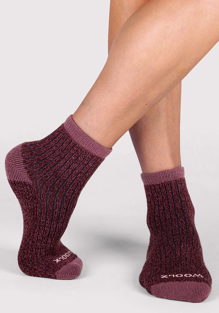 A person wearing Woolx Womens Cozy Mini Crew Sock - Grape Harvest stands on tiptoe on one foot against a light grey background.