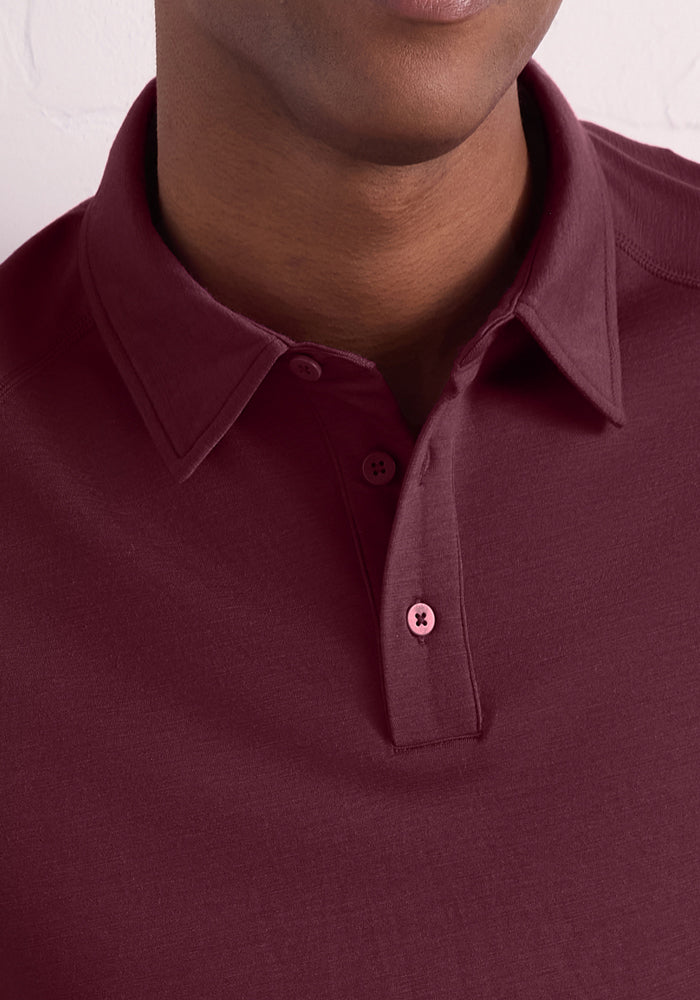 A close-up of a person wearing the Woolx Summit Polo in Grape Harvest, featuring two visible buttons, showing the neck, part of the chin, and upper chest against a plain white wall.