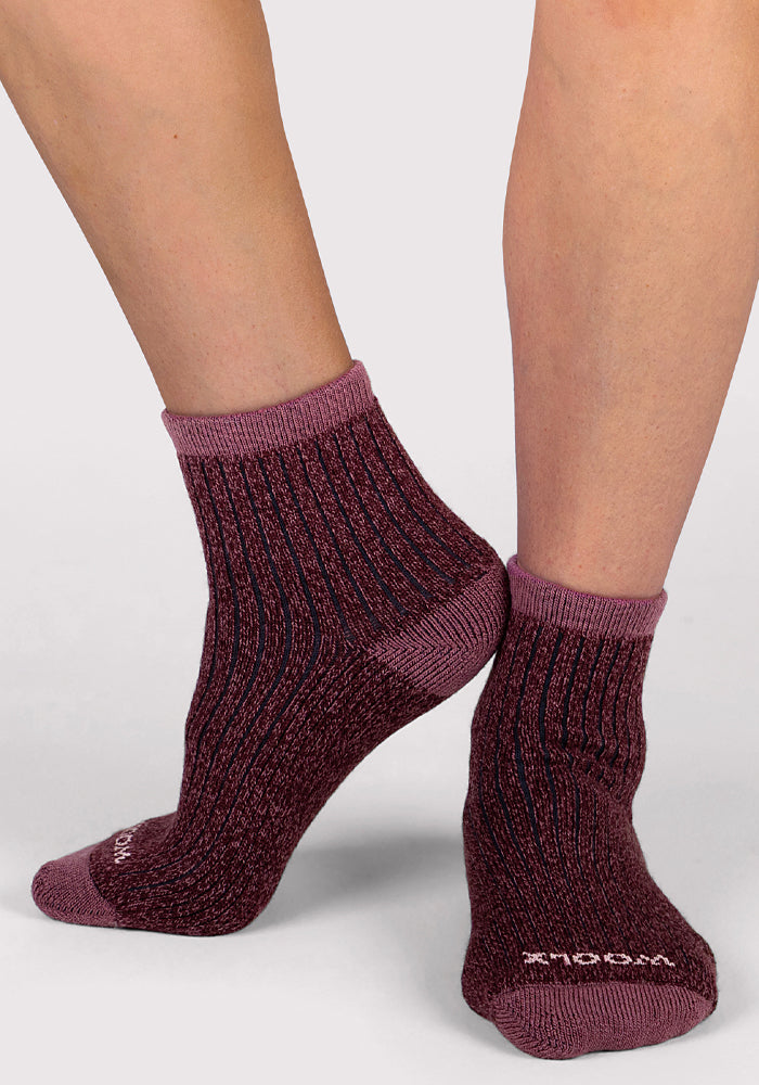 A person wears Woolx Womens Cozy Mini Crew Sock - Grape Harvest, featuring maroon and purple Merino wool with a ribbed, textured knit and contrasting toe and heel. Their crossed feet display these luxury crew socks against a plain light background.
