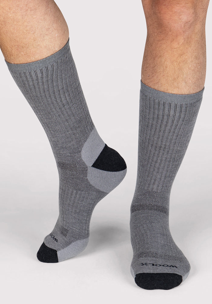 A person stands on a white background wearing Woolx Mens Core Crew Socks in grey, featuring black toes and heels—one foot flat, the other slightly raised.