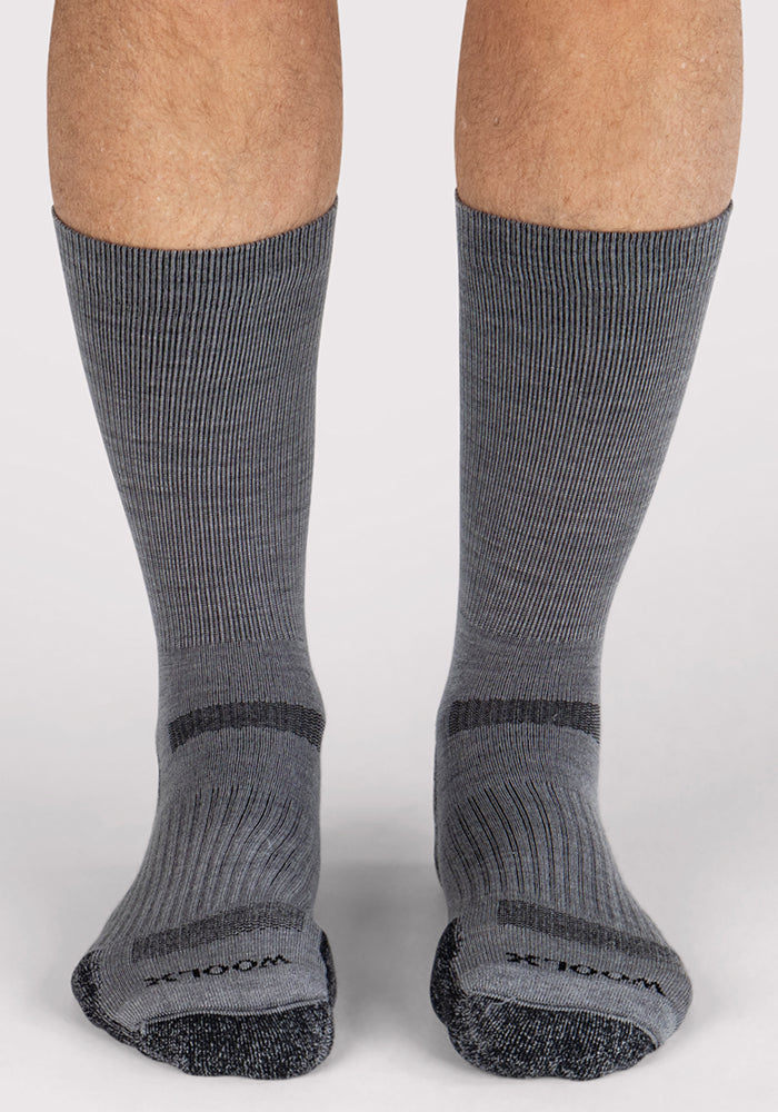 Close-up of feet in Woolx Mens Harbor Crew Sock - Grey, featuring ribbed Merino wool with darker gray heels and toes. These moisture-wicking socks cover mid-shin for all-day comfort and stand on a white surface.