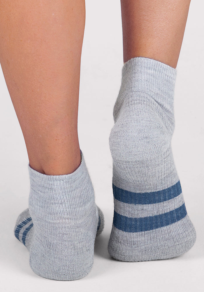 Two feet wear Woolx Womens Rambler Ankle Sock in grey, featuring two dark blue cuff stripes, shown from the back on a white background. These moisture-wicking socks keep your feet dry and comfortable all day.