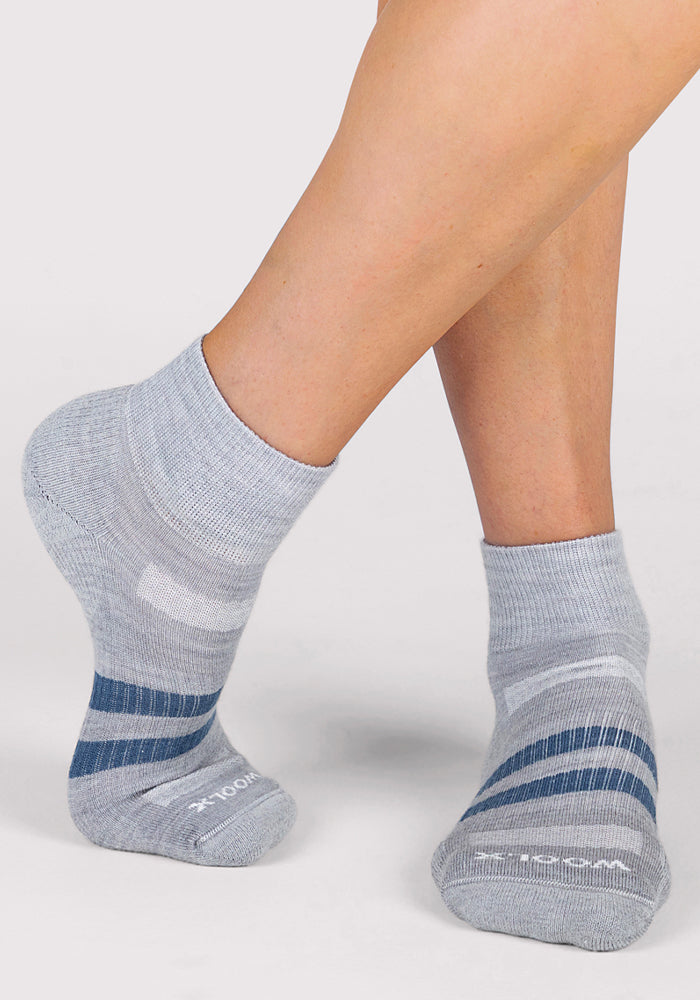 A woman wearing Woolx Womens Rambler Ankle Sock - Grey stands on tiptoes against a plain light background, highlighting the moisture-wicking comfort and striped design of these Merino wool ankle socks.