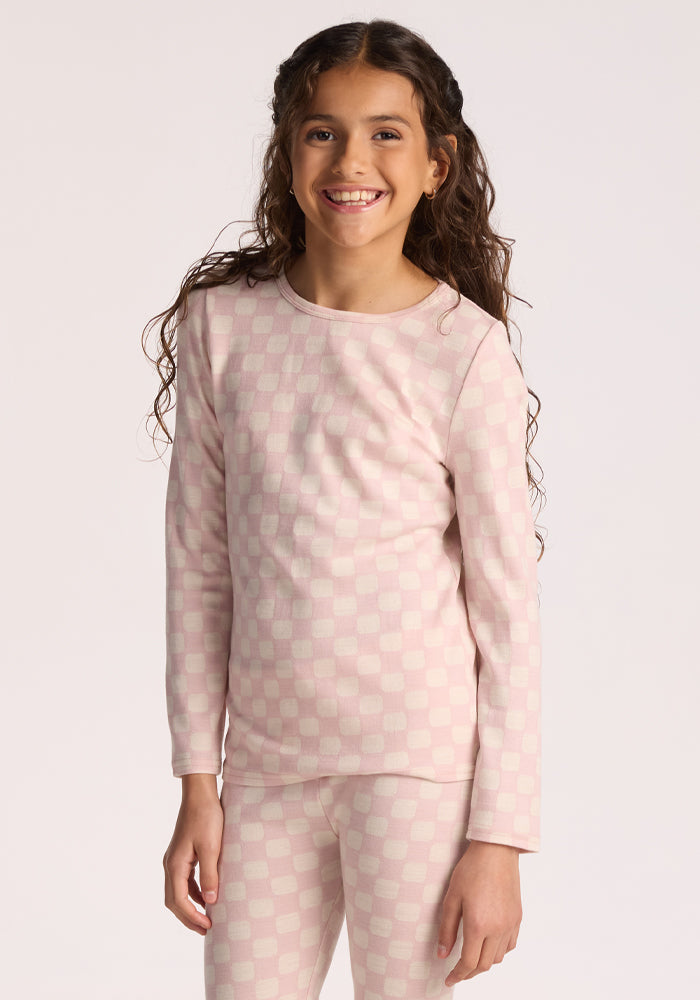 A young girl with long curly hair smiles while wearing the Woolx Kids Explorer Base Layer Top in Hopscotch Pink, standing against a plain light background.