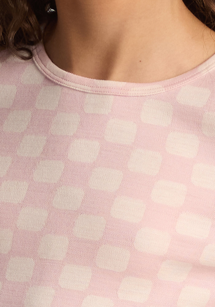 Close-up of a child wearing the Woolx Kids Explorer Base Layer Top in Hopscotch Pink, featuring a light pink and off-white checkerboard pattern, with part of their neck, shoulder, and curly hair visible.
