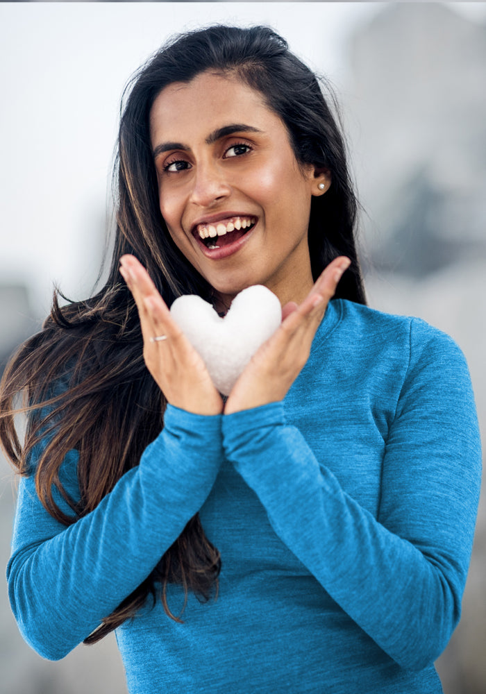 Smiling woman in Woolx’s Hannah Long Sleeve Top - Blue Razz frames a heart-shaped snowball, capturing winter joy.