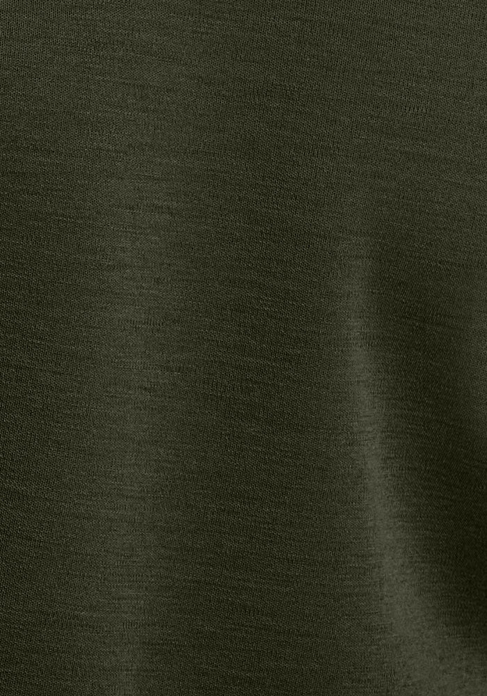 Close-up of Woolx Hannah Long Sleeve Top in Duffel Bag, showing olive Merino wool fabric texture with a soft shadow.