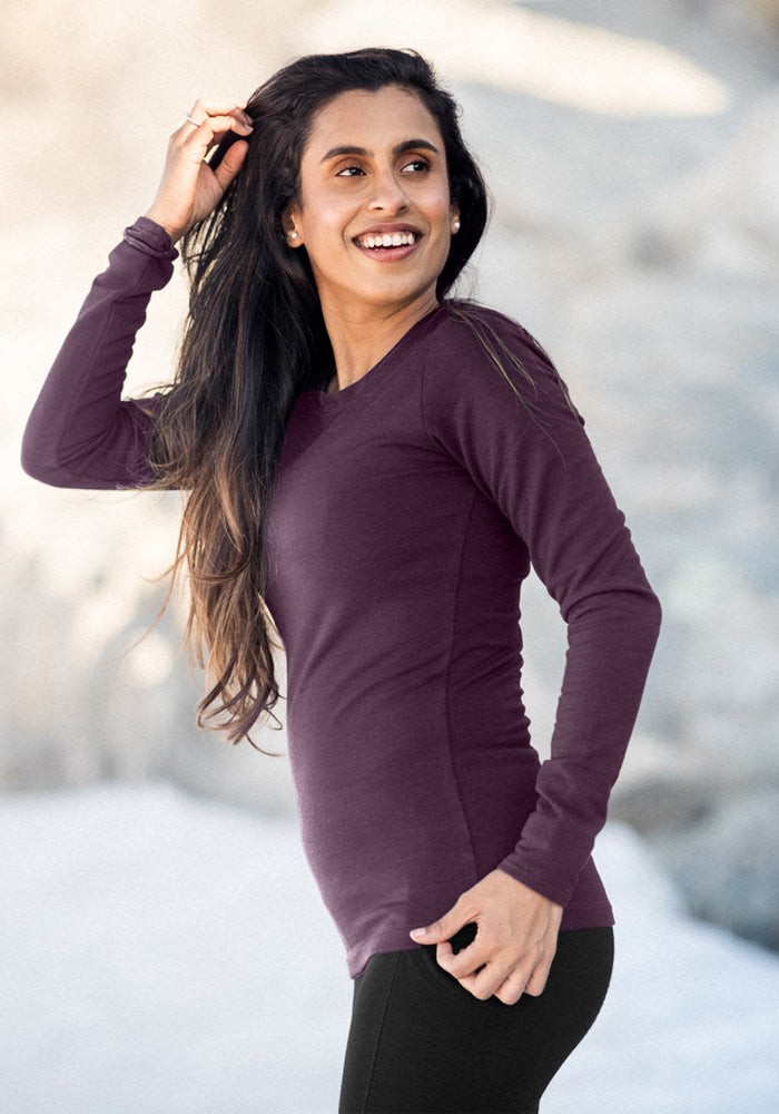 Woman with long dark hair smiles in a Woolx Hannah Long Sleeve Top - Purple Iris and black pants outdoors.