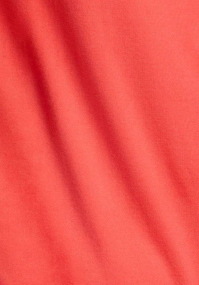 Close-up of Woolx Georgie Dress - Hibiscus, featuring soft coral pink merino wool fabric with subtle shadows and folds.