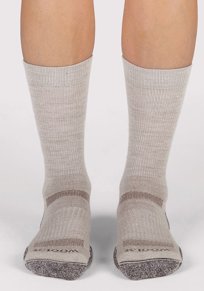 A pair of feet wearing Woolx Womens Harbor Crew Socks in Icicle—light gray and breathable with darker gray toes and heels—stands on a white background.
