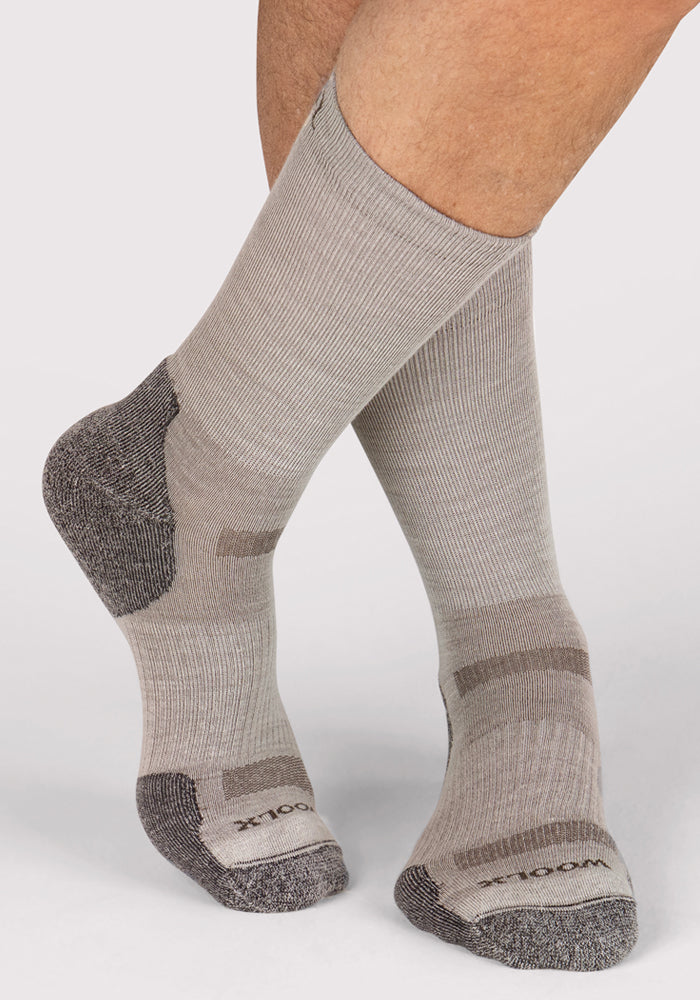 A person stands on a white background wearing Woolx Mens Harbor Crew Sock - Icicle, featuring light gray Merino wool with darker gray heels and toes. “WOOL” appears near the toes, showing these socks' temperature-regulating comfort.