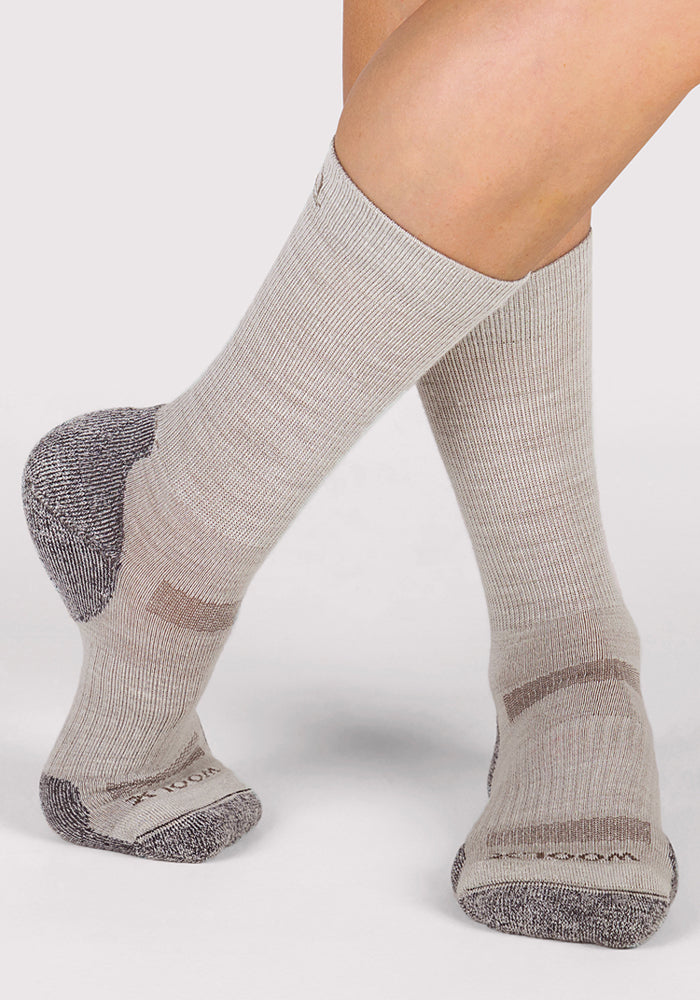 A person wearing Woolx Womens Harbor Crew Socks in Icicle—light gray, breathable crew socks with darker gray toes, heels, and soles—stands on a light background with feet crossed at the ankles.