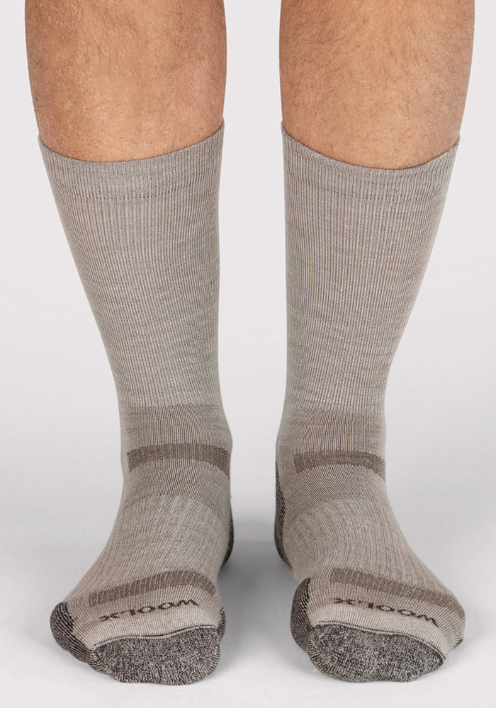 A close-up shows a person’s lower legs and feet wearing Woolx Mens Harbor Crew Sock - Icicle, featuring light gray Merino wool with dark gray accents on toes, heels, and arch. These moisture-wicking socks are set against a plain, light-colored background.