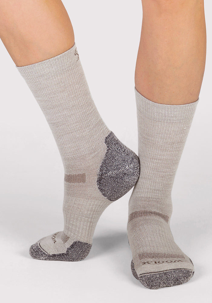 A person wearing Woolx Womens Harbor Crew Sock - Icicle, featuring breathable Merino wool with dark gray heels and toes, stands with one foot slightly raised and the other flat against a plain background.