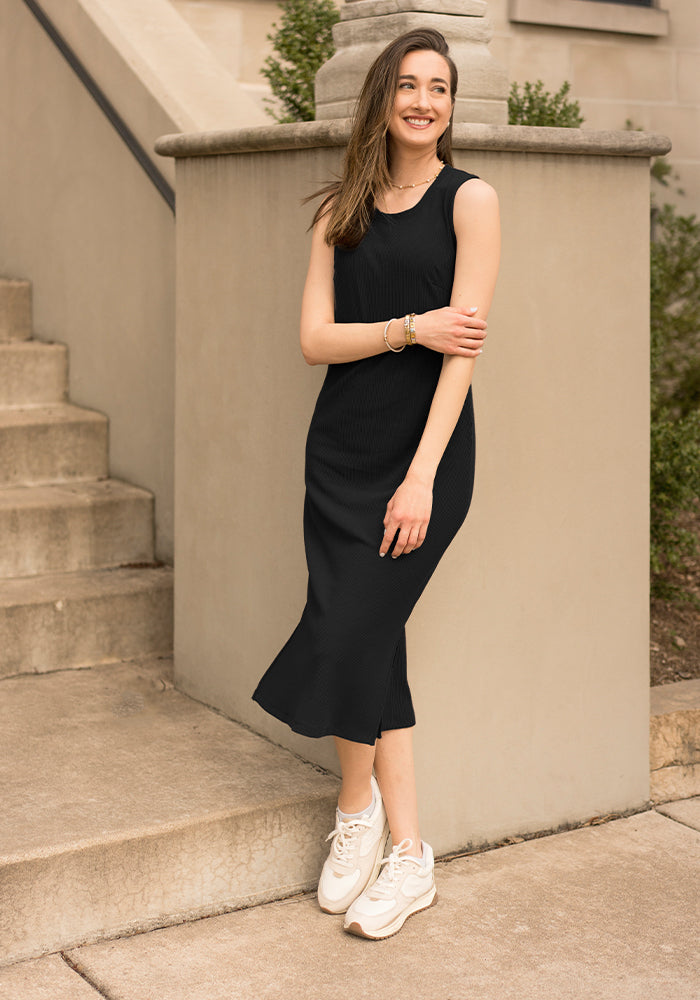Woman wearing the Woolx Iris Ribbed Dress in black with white sneakers, smiling by steps and a stone railing.