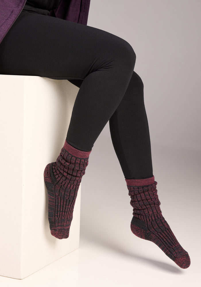 A person in black leggings and Woolx Womens Joey Crew Socks - Warm Violet sits cross-legged on a white block against a plain light grey background.