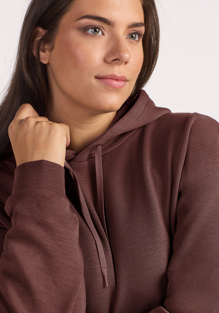 Woman in Woolx Avery Hoodie - Canyon Clay, looking sideways with a neutral expression against a light background.