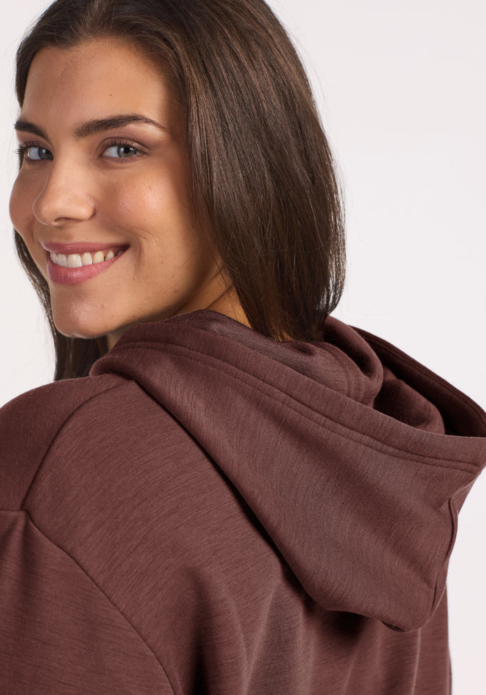 Smiling woman in Woolx Avery Hoodie—Canyon Clay, looking over her shoulder with long brown hair.
