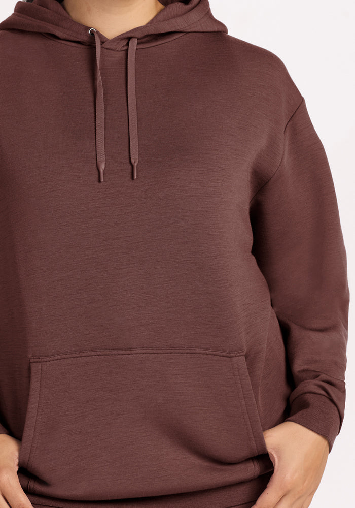 Model in Woolx Avery Hoodie - Canyon Clay, hands in front pocket, showcases this cozy classic on a plain background.