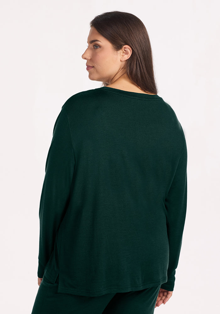 A woman wearing the deep pine Ashlie Lounge Top, a dark green, wrinkle-resistant merino wool travel shirt.